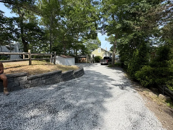 Driveway Excavation & Retaining Wall — Plymouth, MA Graded gravel driveway with segmental block retaining wall after excavation and site work in Plymouth, MA