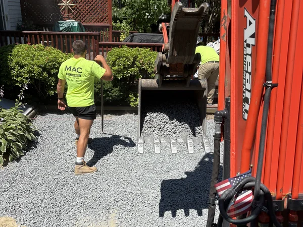Paver Base Installation — East Bridgewater, MA Crew spreading crushed gravel base with a mini excavator during paver hardscape installation in East Bridgewater, MA