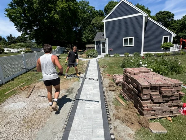 Paver Walkway Installation — Scituate, MA MAC crew installing a porcelain paver walkway with charcoal border in a Scituate, MA backyard