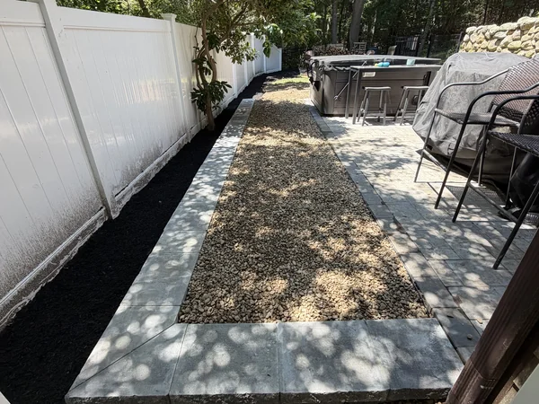 River Rock & Paver Walkway — Marshfield, MA Finished river rock walkway with concrete paver border beside a hot tub patio in Marshfield, MA